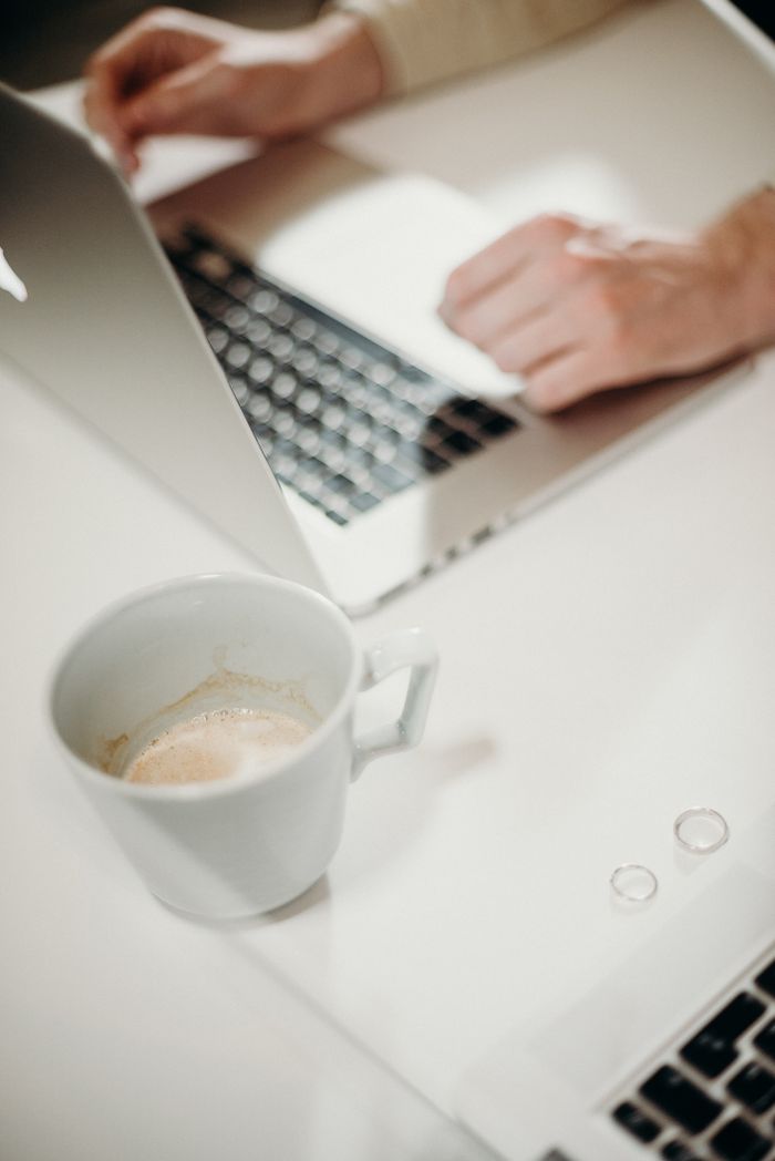 Close-up of hands typing on laptop with coffee cup nearby, creating a casual workspace vibe.