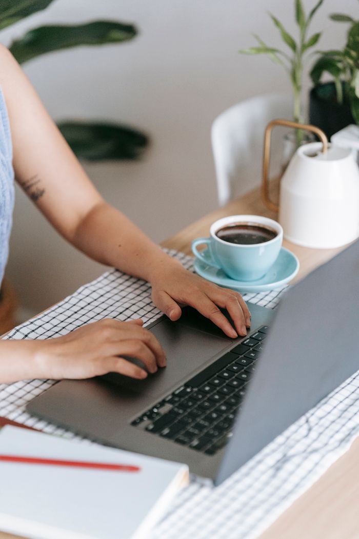Crop unrecognizable freelancer using touchpad of netbook at table on blurred background at home