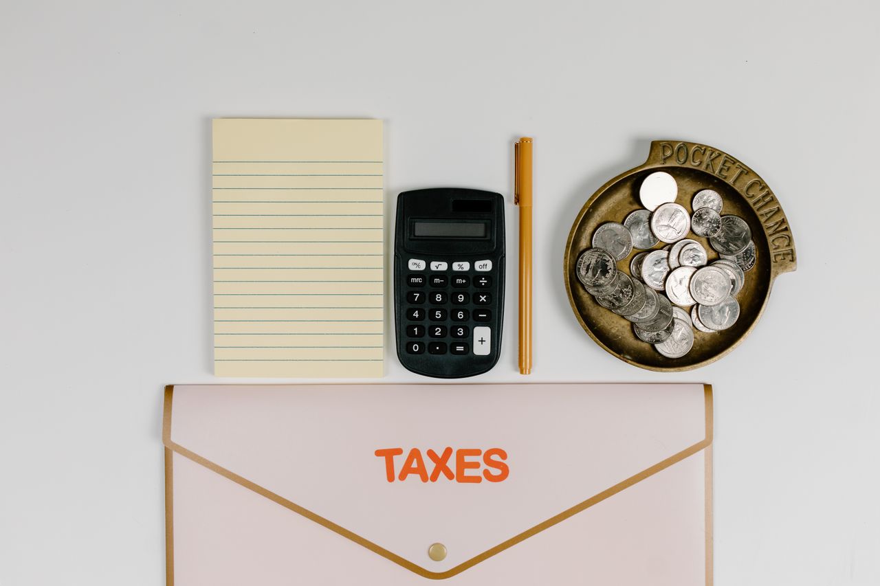 A flat lay of tax preparation essentials: calculator, coins, notepad, pen, and folder.